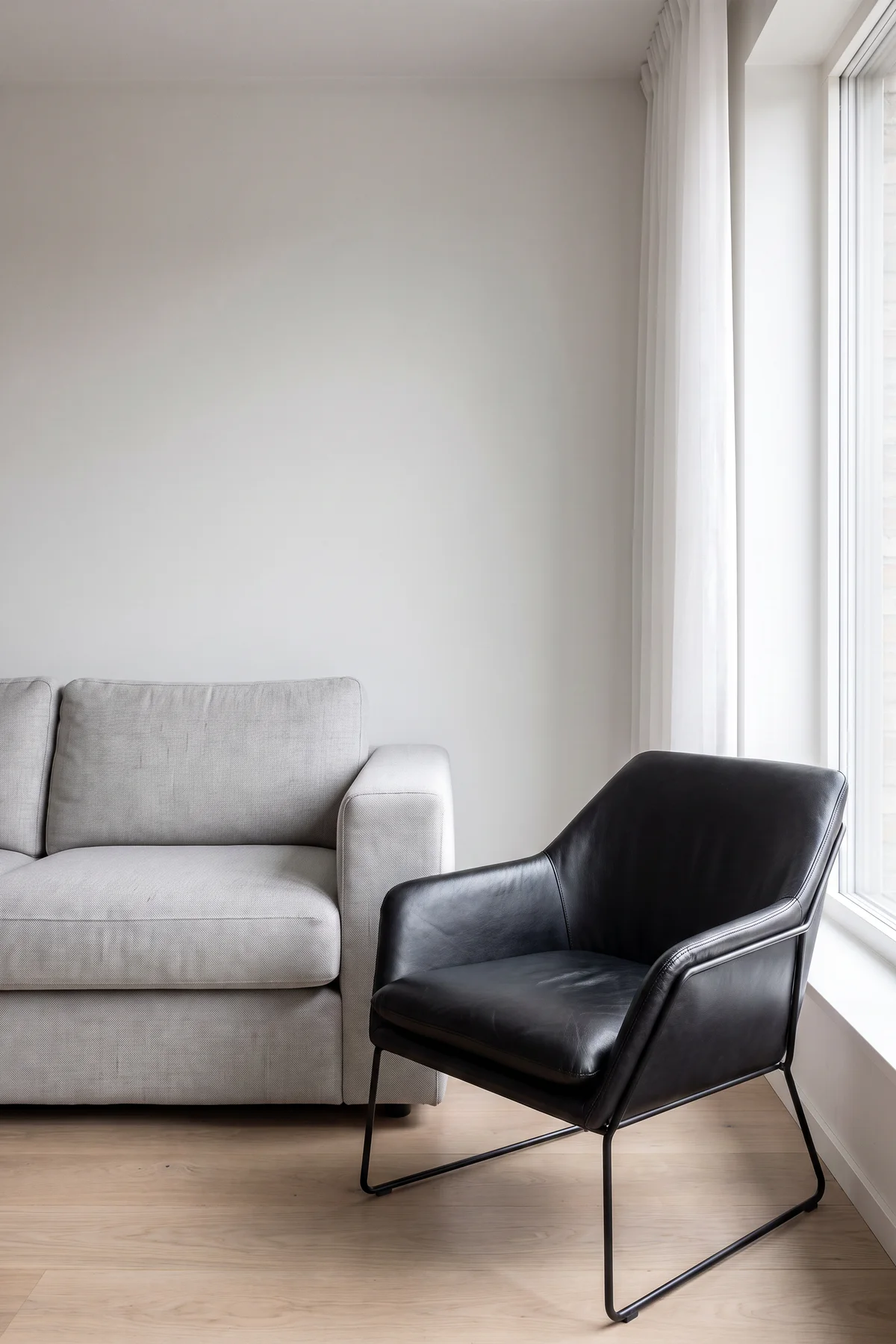 Black leather lounge chair beside the same grey sofa after AI interior object replacement